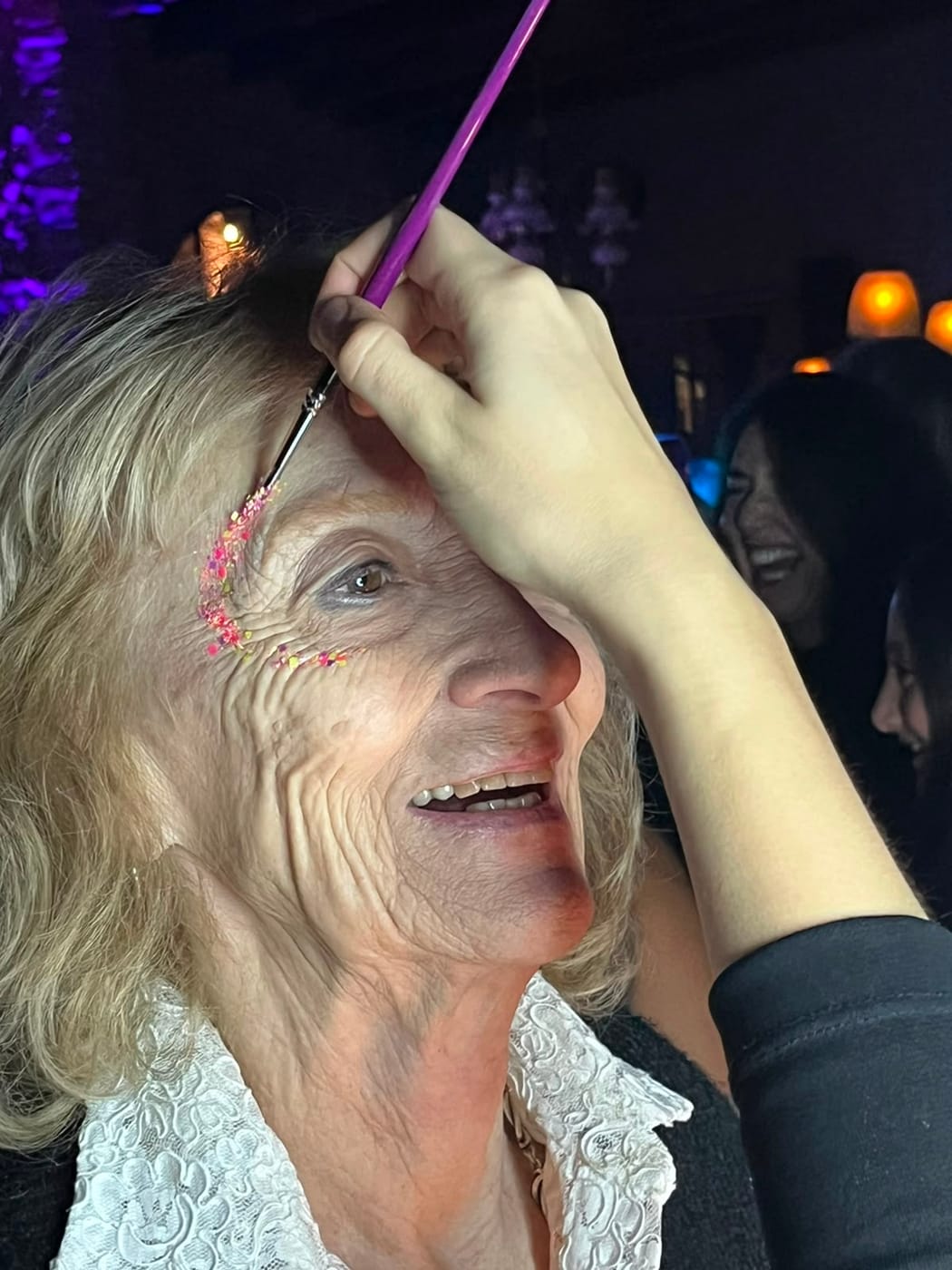 Aplicación de glitter rosa junto al ojo de una invitada sonriente